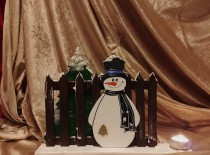 Schneemann vor dem Zaun mit Tannenbaum und Kerze